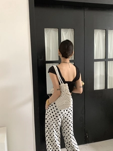 Detailed view of white woven bucket bag styled with black backless top and polka dot pants