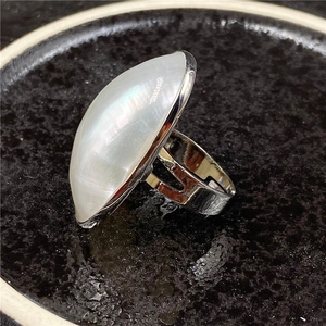 Macro view of a large oval mother of pearl ring with silver adjustable band on black tray