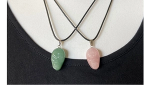 Detailed view of light green and pink crystal skull pendants on black cords