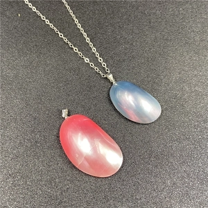 Détail de pendentifs en perles Mabe bleues et rouges sur chaîne argentée et fond gris