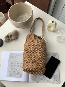 Draufsicht auf Stroh-Eimertasche mit Kordelzug-Innenfutter und dekorativen Accessoires