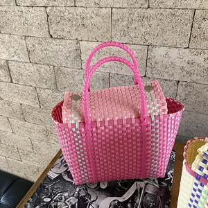 Sac panier en PVC tissé rose avec accents verts sur fond de bois vintage