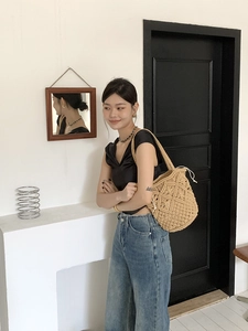 Detailed outdoor view of a hand-woven hollow straw shoulder bag with white drawstring liner