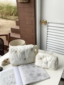 Close-up of two quilted cosmetic bags with gold rabbit embroidery and zipper details