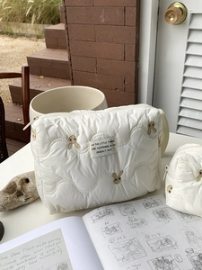 Detail of white quilted cosmetic bags with brown rabbit embroidery and top zipper closure