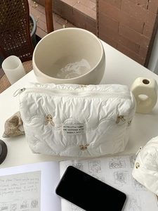 Detail of white quilted cosmetic bag featuring embroidered gold rabbit and zipper closure