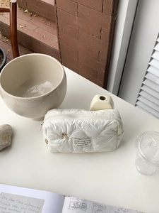 Detail of white quilted cosmetic bag with embroidery and bear patch on desk