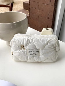 Detail of white quilted cosmetic bag with bunny embroidery and orderly life quote label