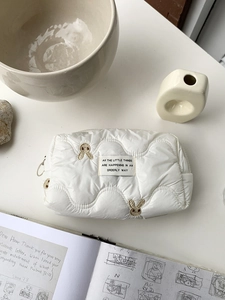 Close-up of quilted white makeup bag with bunny embroidery and soft wave texture