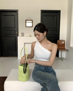 Nahaufnahme eines weißen One-Shoulder-Stricktops mit Rüschen und grüner gewebter Handtasche
