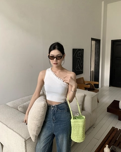 Detail einer grünen Stroh-Eimertasche mit weißem Spitzen-Trägertop und Jeans-Outfit