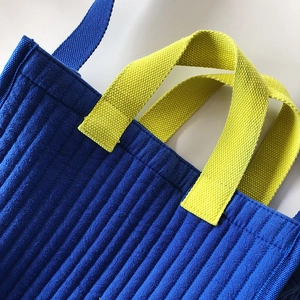 Close-up of quilted navy tote bag showing yellow straps and precise vertical stitching