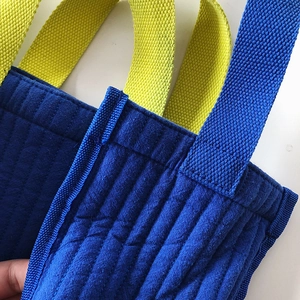 Close-up of reinforced stitching on blue quilted canvas tote bag with yellow straps