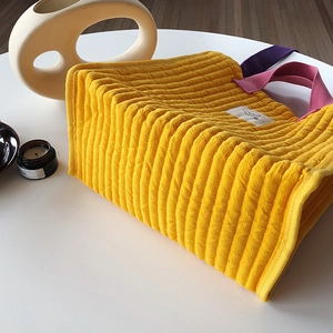 Detailed shot of yellow quilted tote bag with contrast handles and smiley patch on table