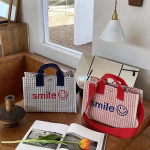Dettaglio ricamo sorriso su borse tote in tela blu navy e rosse in ambiente accogliente
