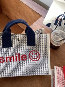 Dettaglio del ricamo smile rosso e chiusura magnetica su borsa in tela beige