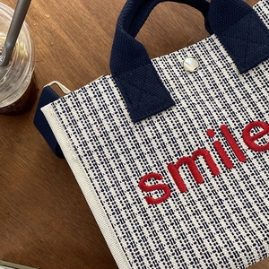 Borsa tote in tela con ricamo smile rosso e manici blu scuro su tavolo di legno