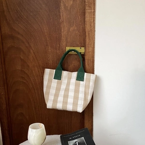 Canvas tote bag with khaki stripes hanging on a door handle near a coffee cup and book