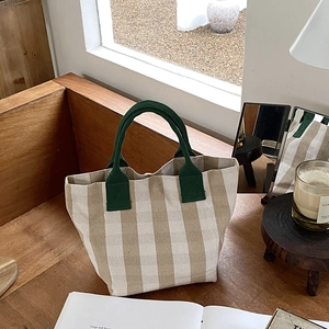 Close-up of vintage striped canvas tote bag with green handles on a wooden table
