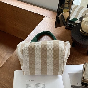 Close-up of a striped canvas tote bag with green handles on a wooden table setup