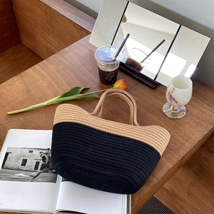 Détail du sac à main bicolore en coton tressé sur une table de café en bois