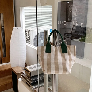 Close-up of canvas tote bag with green handles hanging on a modern glass door handle