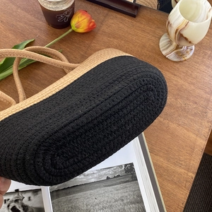 Détail d'un panier tressé bicolore en corde de coton posé sur une table en bois naturel