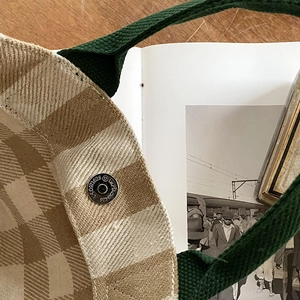 Detail of grid fabric tote bag showing tight stitching and magnetic closure on wood desk