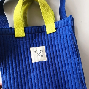 Quilted blue tote bag with yellow handles and cute sheep patch on a white background