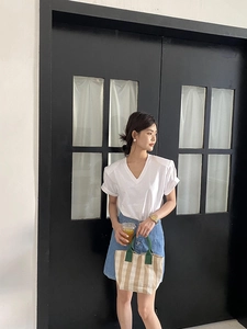 Detail of a minimalist checkered tote bag styled with a white V-neck shirt and denim skirt