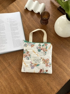 Petit sac matelassé beige avec oursons et fermeture éclair verte sur un bureau en bois
