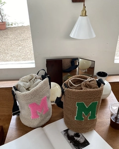 Detail of plush lamb wool bucket bags with drawstring and M letter patch in indoor setting