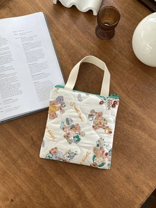 Détail d'un sac à main matelassé crème avec motif ours et fermeture éclair verte sur bois