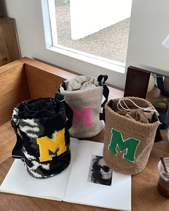 Detailed view of plush drawstring bucket bags with letter M patches on a wooden table