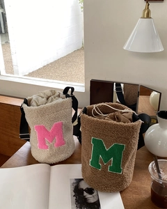 Detail of plush bucket bags in beige and brown with letter embroidery on a desk