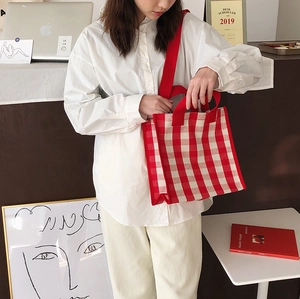 Detail of red and white plaid tote bag shown in a lifestyle scene with shoulder strap