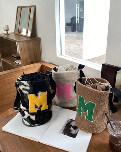 Close-up of plush bucket bags in various colors featuring embroidered letter M detail