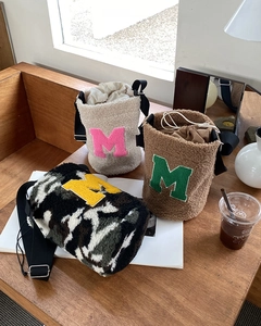 Detailed view of plush teddy fabric bucket bags with M embroidery and wide straps