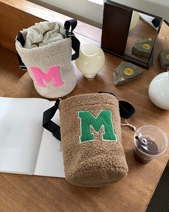 Detail of plush lamb wool bucket bags with M letter embroidery on a wooden table