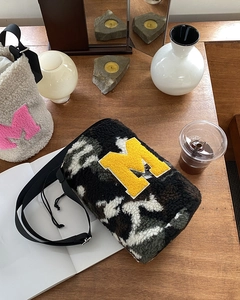 Detail of plush lamb wool bucket bag with letter M patch and adjustable nylon strap