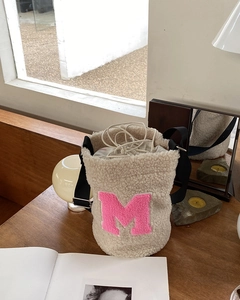 Detail of beige fleece bucket bag with pink M letter patch and drawstring closure