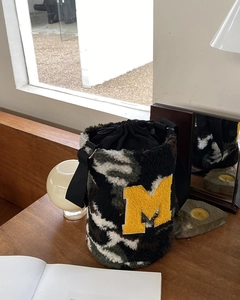 Detail of plush camouflage bucket bag featuring yellow M patch and black drawstring closure