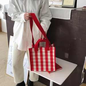 Detail view of red and white plaid knit tote bag with shoulder strap and short handles