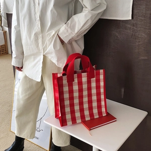 Detail of red and white checkered canvas tote bag with wide webbing handles on a white table