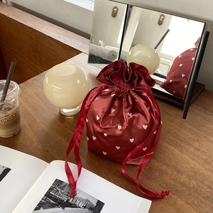 Close-up of a burgundy satin drawstring pouch with heart patterns on a wooden table