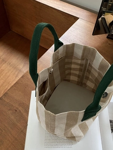 Checkered canvas tote bag with green handles and magnetic closure in lifestyle scene