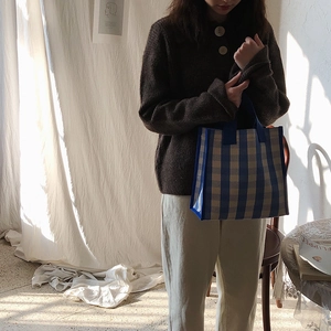 Blue and beige checkerboard tote bag shown in a cozy lifestyle setting with soft lighting