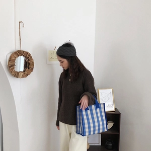 Blue and white checkered canvas tote bag styled with casual knitwear in a minimalist setting