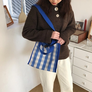 Blue and white checkered knit tote bag with shoulder strap in cozy home interior setting