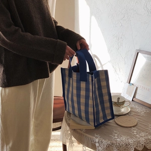 Detail of blue and white checkered tote bag featuring durable wide woven handles